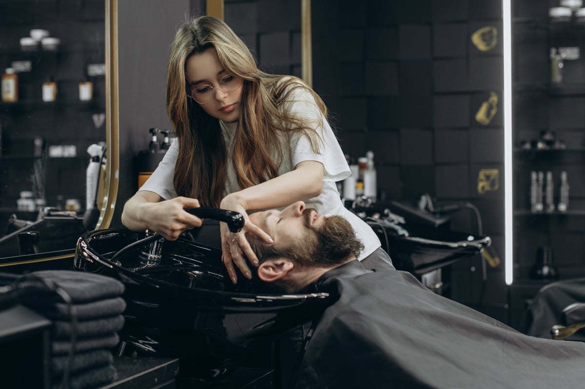 Professional barber washing client's hair at a modern salon sink